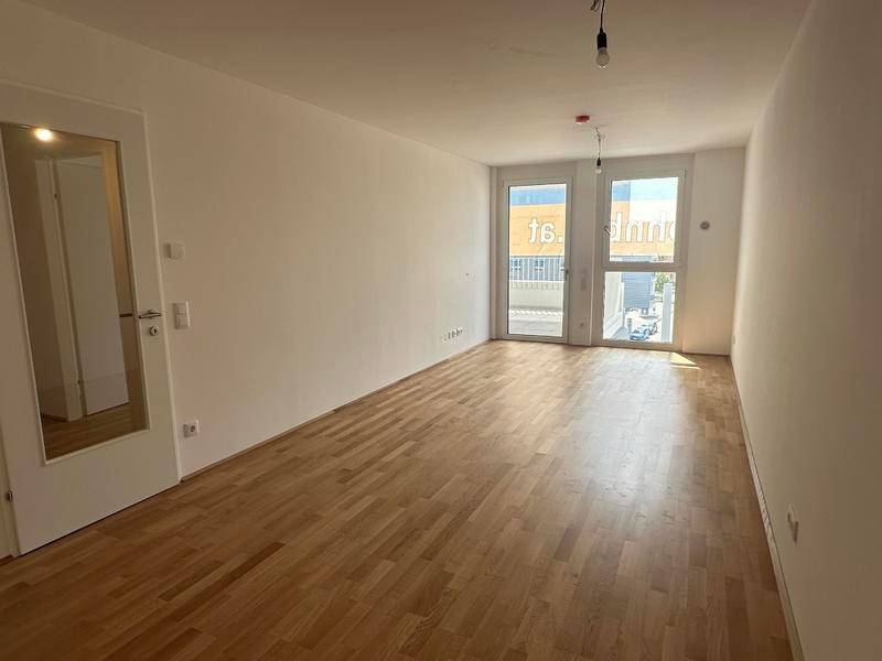 Heller, leerer Raum mit Holzboden und Zugang zu einem Balkon, ideal für Wohnzwecke.