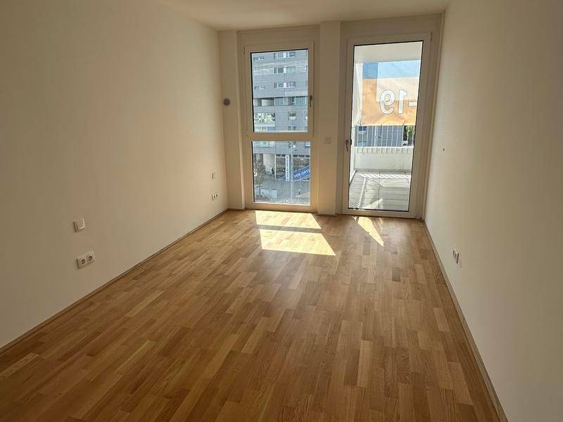 Helles Schlafzimmer mit Holzboden und großem Fenster, das viel Tageslicht hereinlässt.