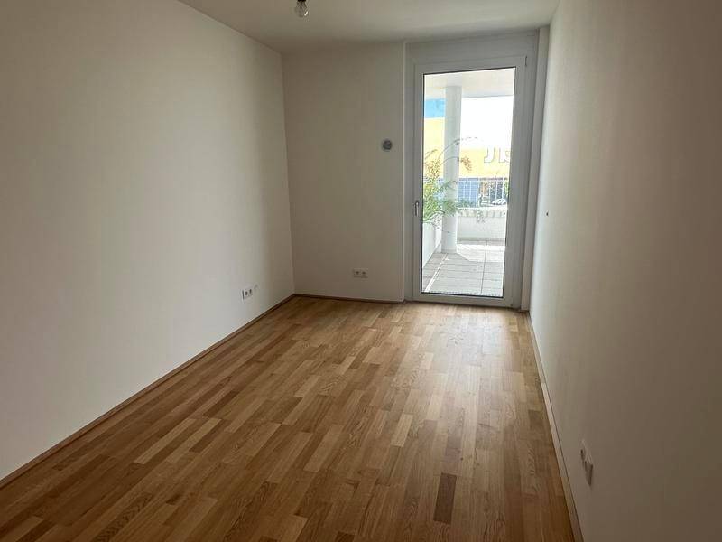 Geräumiges Schlafzimmer mit Holzboden und Balkonzugang, bietet viel natürliches Licht.