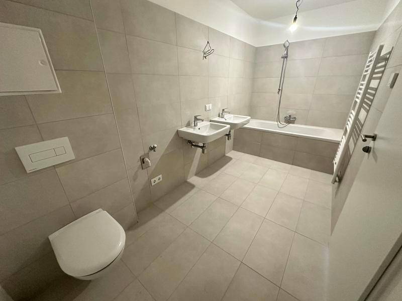 Modernes Badezimmer mit Badewanne, Doppelwaschbecken und Wand-WC, komplett gefliest.