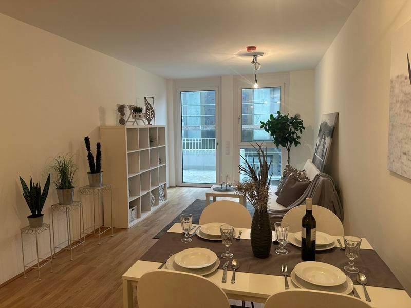 Heller Wohn- und Essbereich mit Holzboden, modernem Esstisch und Zugang zum Balkon.