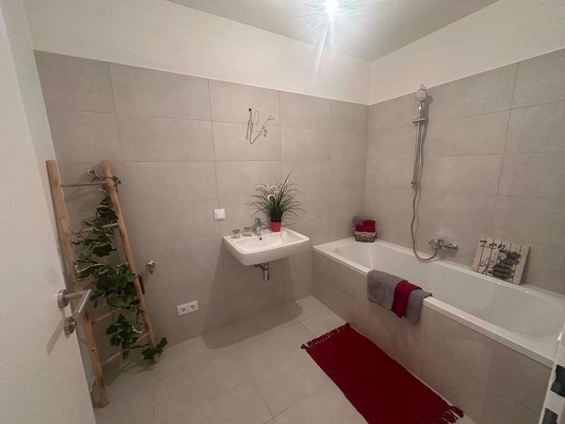 Modernes Badezimmer mit Badewanne, Waschbecken und hellen Fliesen, funktional eingerichtet.