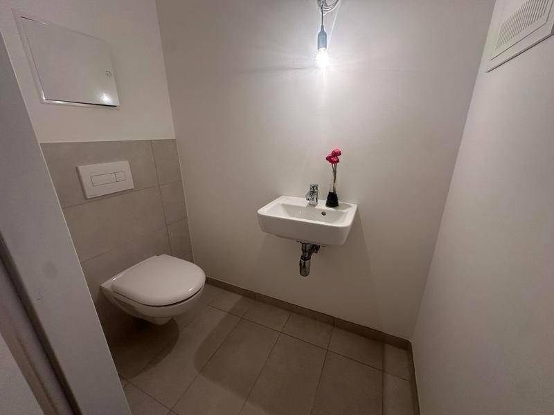 Kleines Gäste-WC mit wandhängender Toilette und Handwaschbecken, hell gefliest.