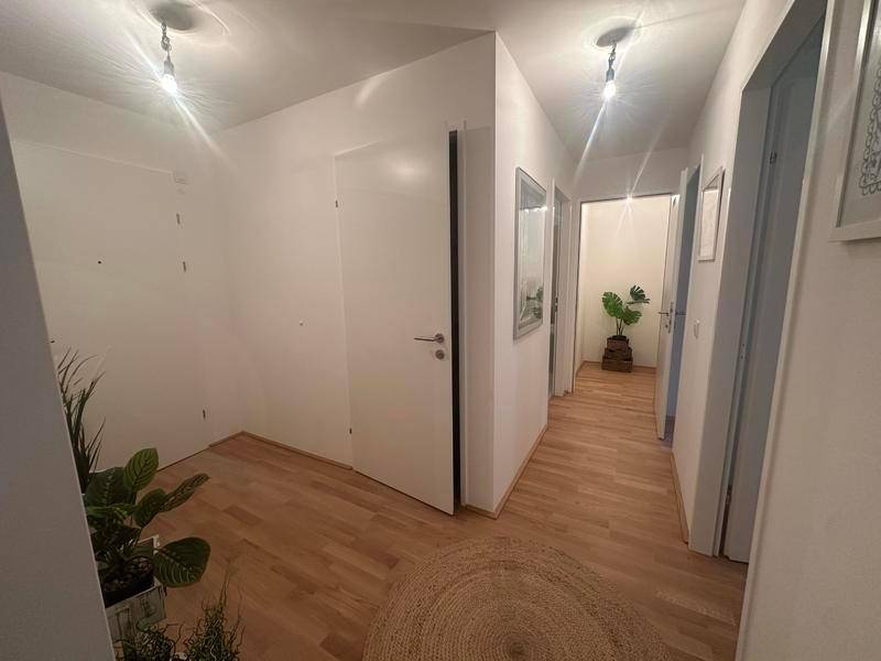 Heller Flur mit Holzboden und weißen Wänden, der zu weiteren Räumen führt.