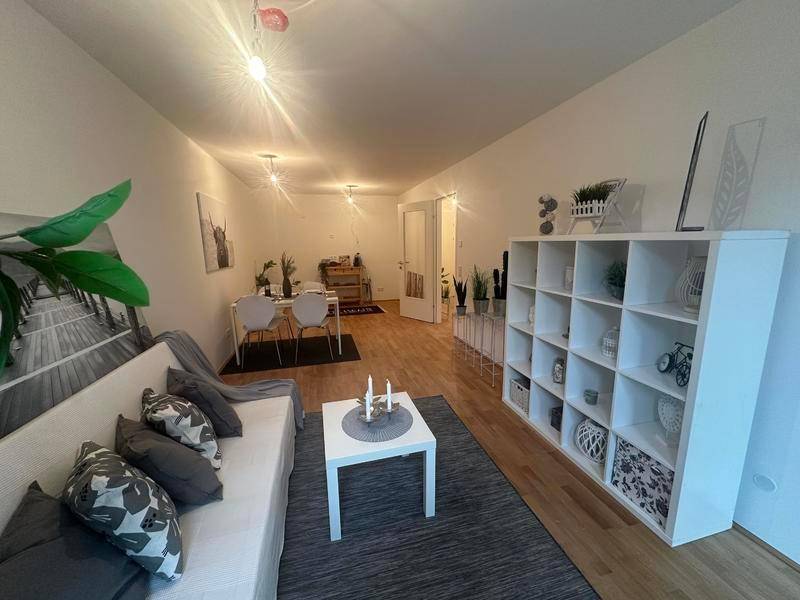 Gemütliches Wohnzimmer mit hellem Sofa, Teppich und weißem Regal, gut beleuchtet.