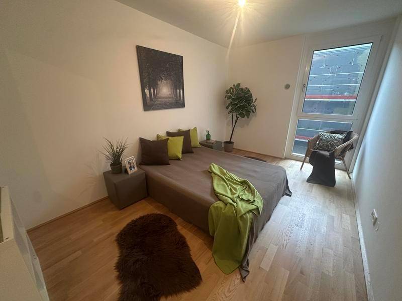 Schlafzimmer mit Holzboden, großem Fenster und minimalistischer Einrichtung, gut beleuchtet.