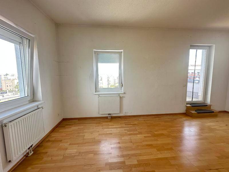 Leerer Raum mit Parkettboden, mehreren Fenstern und viel Tageslicht, bereit zur individuellen Gestaltung.