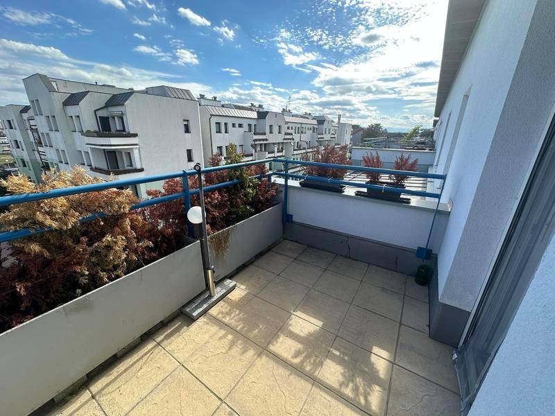 Geräumiger Balkon mit Fliesenboden und Blick auf die umliegenden Gebäude und den Himmel.