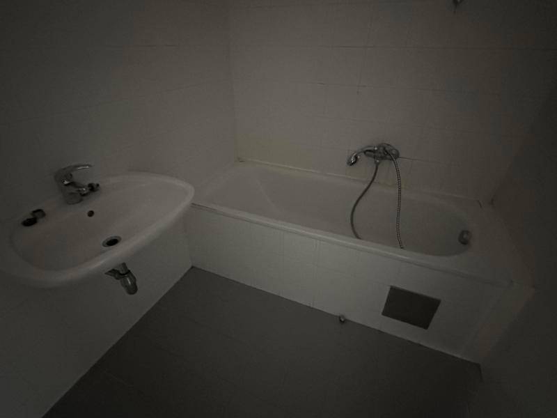 Dunkles Badezimmer mit Badewanne und Waschbecken, die Beleuchtung ist derzeit ausgeschaltet.