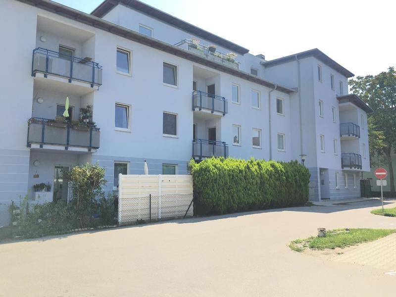 Vorderansicht eines Wohnhauses mit hellgrauer Fassade, Balkonen und gepflegten Hecken im Vorgarten.