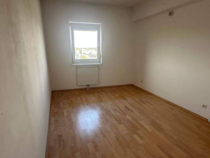 Helles Schlafzimmer mit Parkettboden und einem Fenster, das viel natürliches Licht hereinlässt.