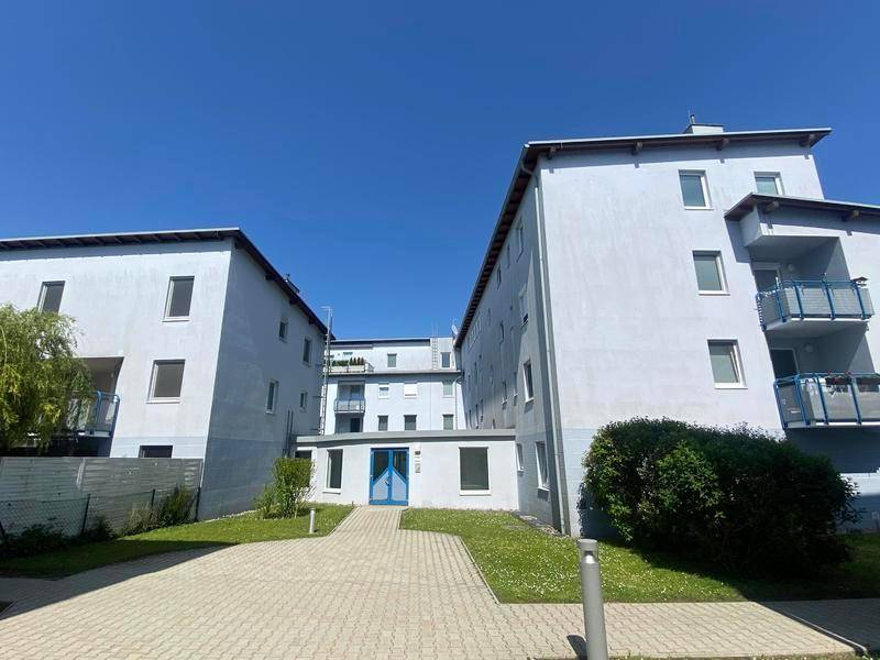 Eingangsbereich eines Wohnkomplexes mit gepflastertem Weg, Rasenflächen und blauer Eingangstür.
