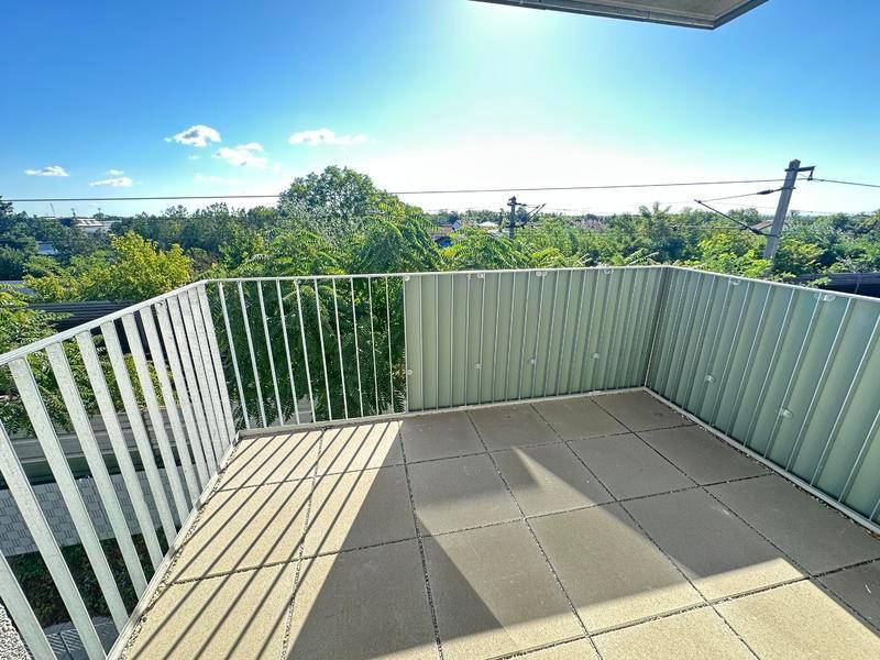 Heller Balkon mit Fliesenboden und Metallgeländer, umgeben von grünen Bäumen unter blauem Himmel.