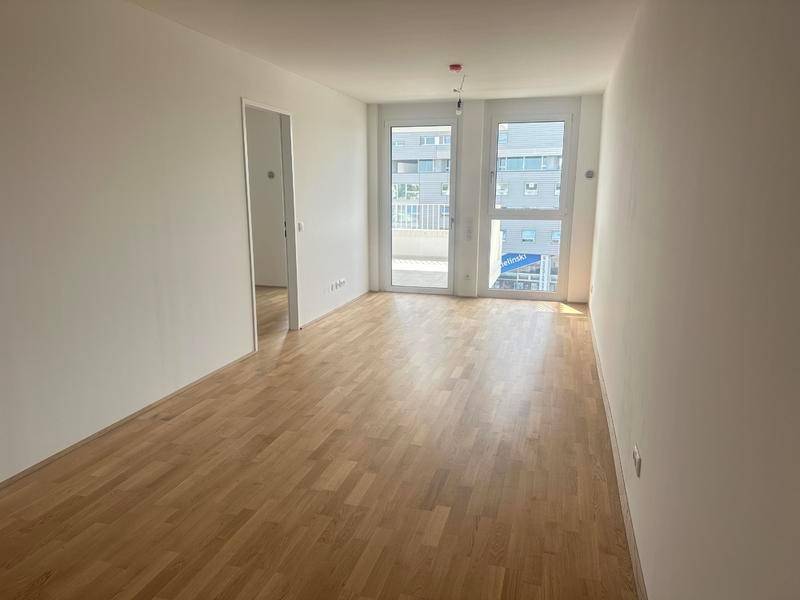 Heller, leerer Raum mit Holzboden und Zugang zu einem Balkon, ideal als Wohnzimmer.