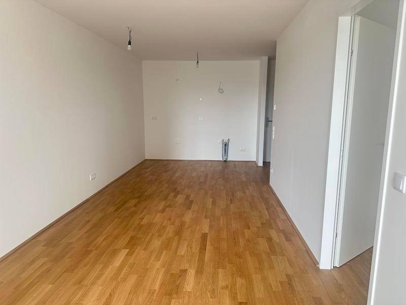 Leerer Küchenraum mit Holzboden und Anschlüssen für eine Einbauküche, bereit zur Gestaltung.