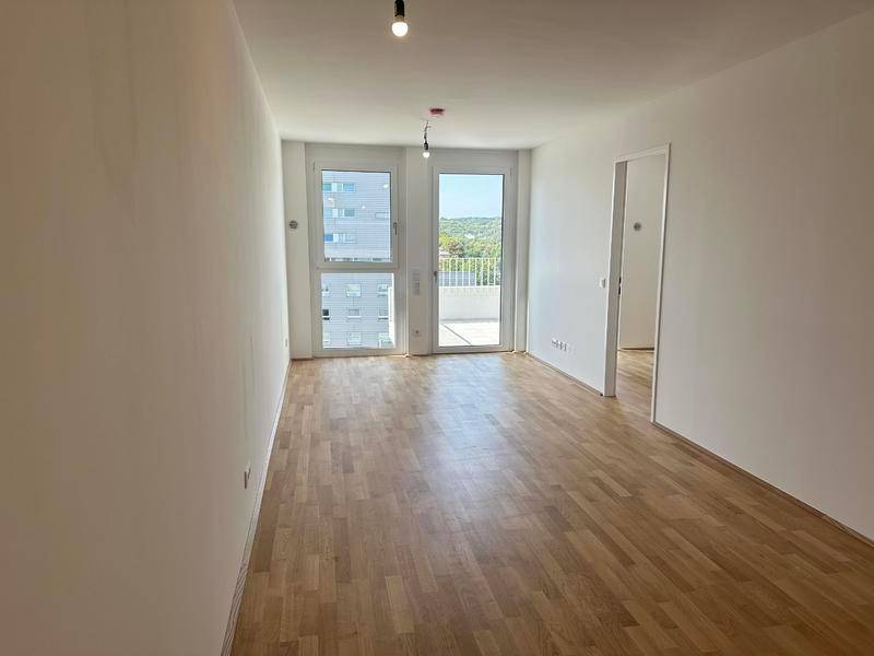 Heller, leerer Wohnraum mit Holzboden und Zugang zu einem sonnigen Außenbereich.
