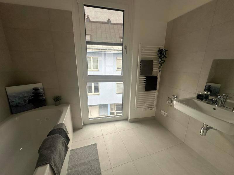 Modernes Badezimmer mit Badewanne, Waschtisch, beheiztem Handtuchhalter und Fenster.