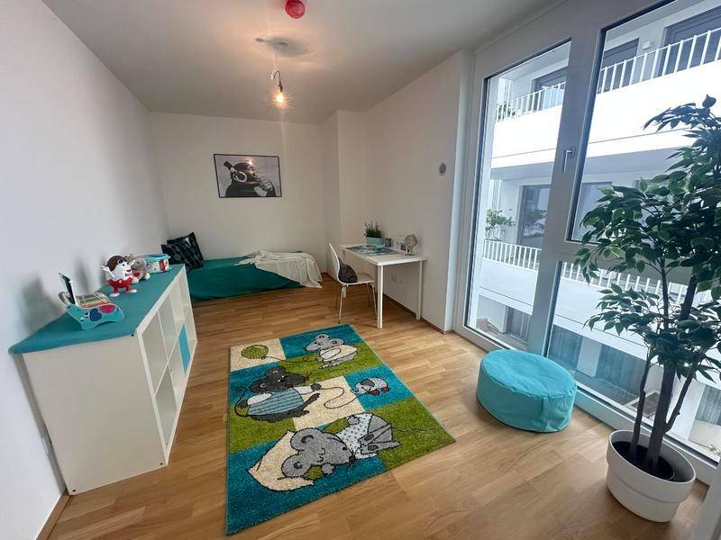 Helles Kinderzimmer mit Holzboden, großem Fenster und bunter Dekoration.