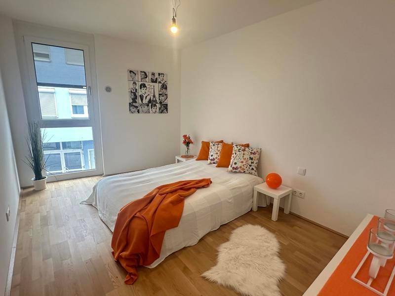 Helles Schlafzimmer mit Holzboden, großem Fenster und moderner Dekoration in Orange.