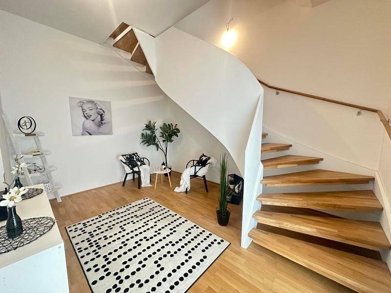 Heller Wohnbereich mit eleganter Wendeltreppe, Holzboden und moderner Schwarz-Weiß-Dekoration.