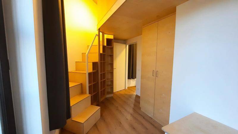 Heller Flur mit Holztreppe und integrierten Regalen, der zu einem oberen Bereich führt.