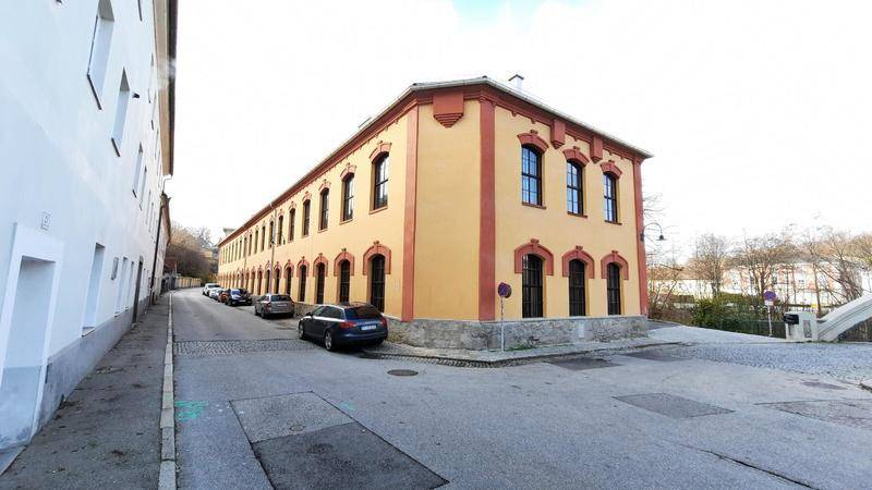 Historisches Gebäude mit gelber Fassade und roten Akzenten an einer ruhigen Straße.