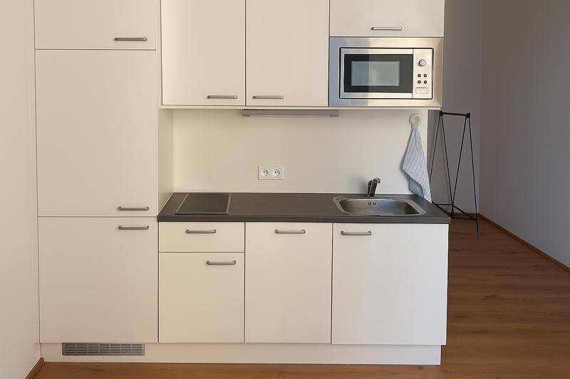 Kompakte, moderne Küchenzeile mit weißen Schränken, integrierter Mikrowelle und Induktionskochfeld.