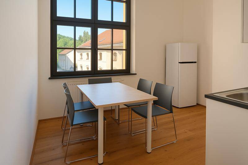 Heller Essbereich mit Tisch und Stühlen neben einem großen Fenster mit Ausblick ins Grüne.