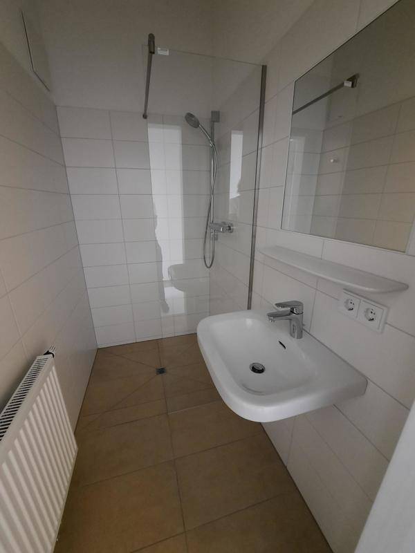 Modernes Badezimmer mit Duschbereich, Waschbecken und weißen Fliesen, funktional und hell gestaltet.