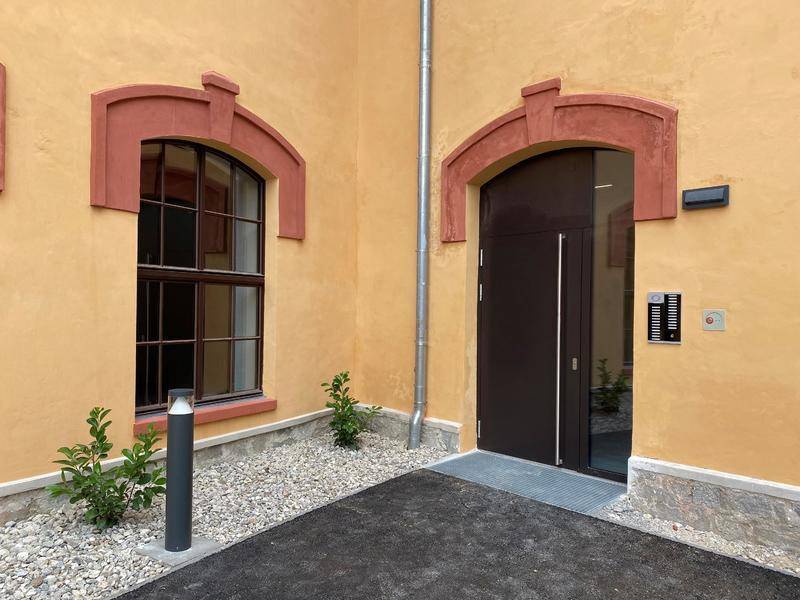 Eingangsbereich eines Gebäudes mit gelber Fassade, Bogenfenster und moderner Eingangstür.