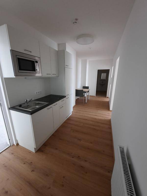 Moderne Küchenzeile mit weißen Schränken, Mikrowelle und Laminatboden, offen zum Wohnbereich.