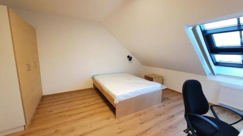 Helles Schlafzimmer im Dachgeschoss mit Schrank, Bett und Schreibtisch unter einem großen Dachfenster.