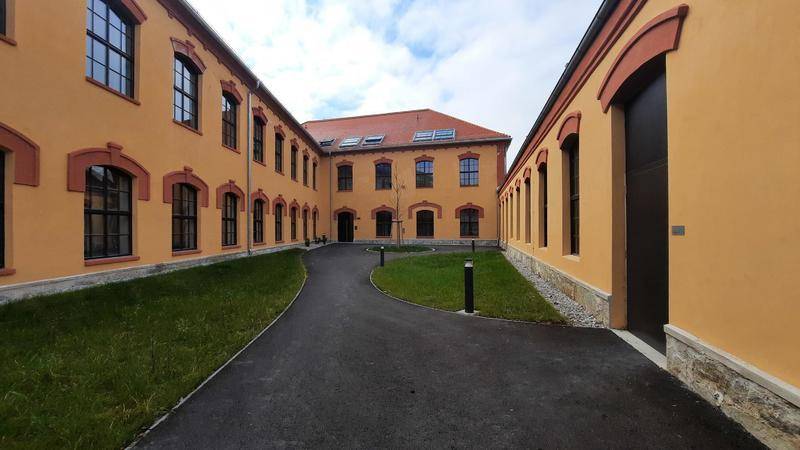 Innenhof eines renovierten Gebäudes mit gelben Fassaden, Grünflächen und einem gepflasterten Weg.