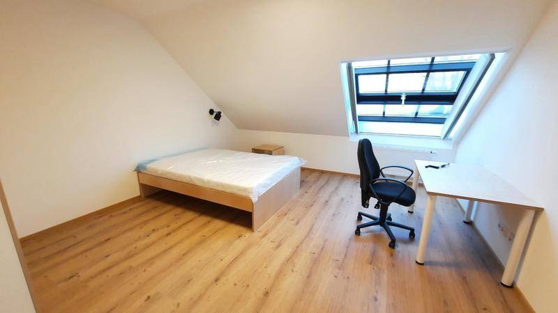 Helles Schlafzimmer im Dachgeschoss mit schräger Decke, Laminatboden, Bett und Schreibtisch unter einem Dachfenster.