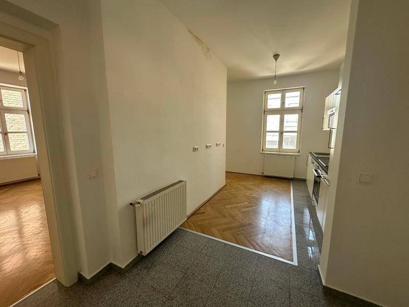 Eingangsbereich mit Fliesenboden, der in einen Raum mit Fischgrätparkett übergeht.