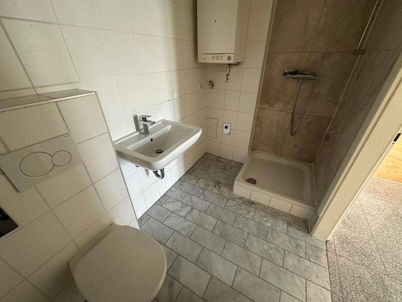 Funktionales Badezimmer mit Dusche, WC, Waschbecken und hellen Fliesen.