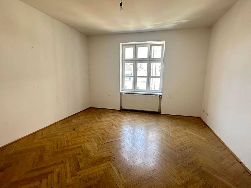 Geräumiger, heller Raum mit klassischem Fischgrätparkett und einem großen Fenster.