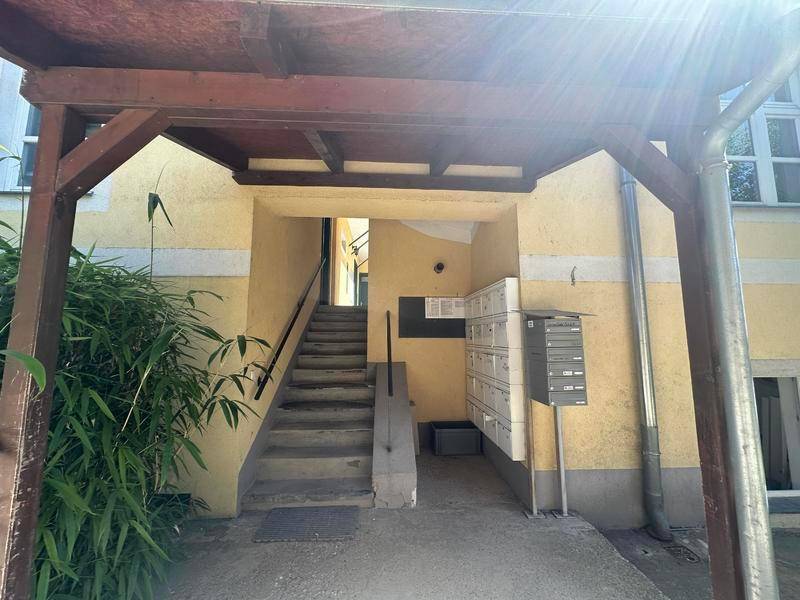 Eingangsbereich eines Gebäudes mit Treppe, Briefkästen und überdachtem Zugang.
