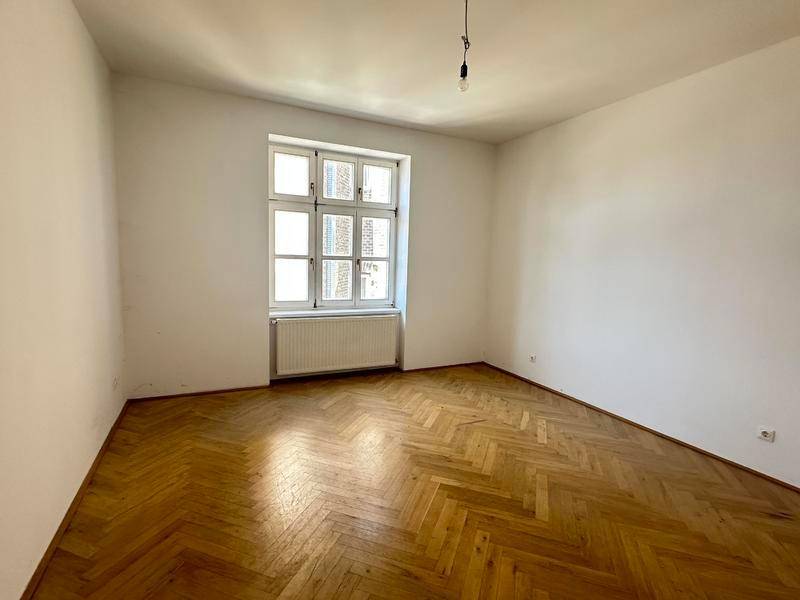 Heller Raum mit Fischgrätparkettboden und einem großen Fenster, bereit zur Einrichtung.