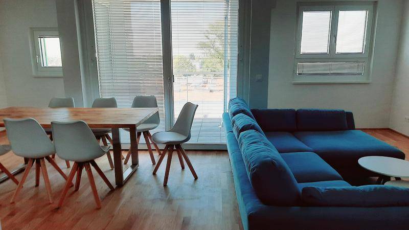 Gemütlicher Wohn-Essbereich mit blauem Sofa, Holztisch und Zugang zur Terrasse.