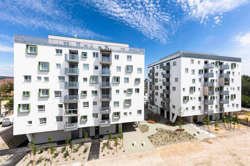 Moderne Wohngebäude mit weißer Fassade, grünen Akzenten und Balkonen unter blauem Himmel.
