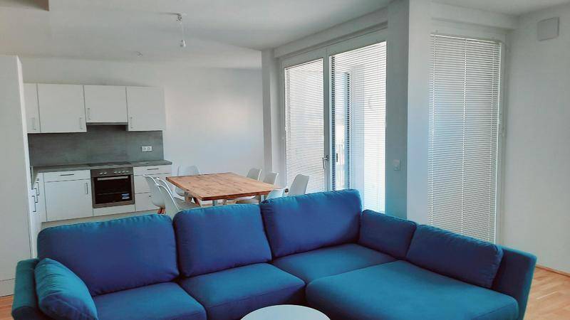 Heller Wohnbereich mit blauer Couch, Esstisch und offener Küche.