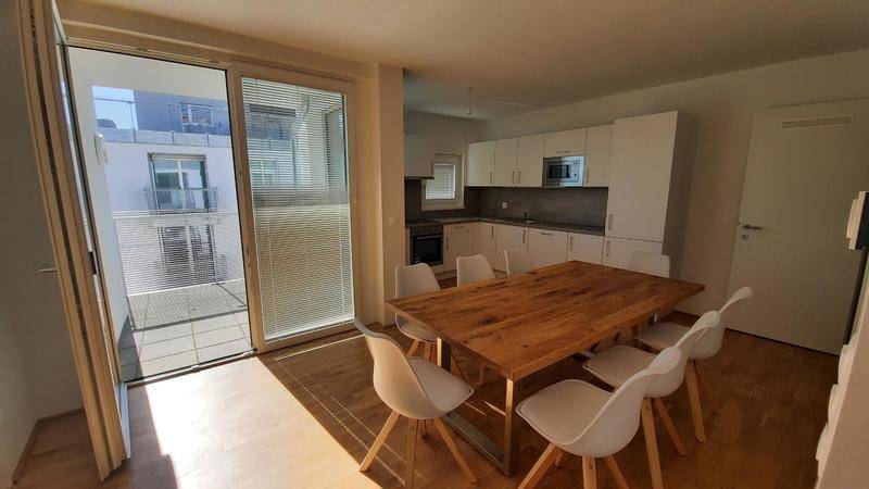 Moderne Küche mit Esstisch, weißen Schränken und Zugang zu einem Balkon.