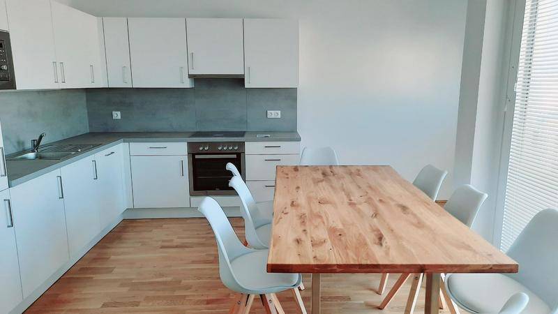 Moderne Einbauküche mit hellem Holztisch, weißen Schränken und Induktionskochfeld.