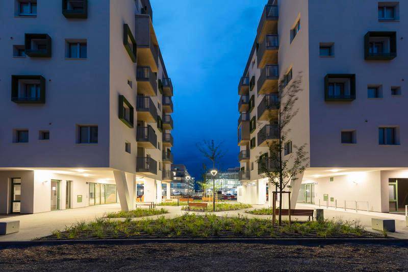 Moderne Wohngebäude mit Balkonen und einem begrünten Innenhof bei Dämmerung.