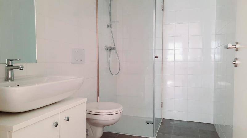 Modernes Badezimmer mit weißer Fliesenwand, Duschkabine und Einzelwaschbecken.
