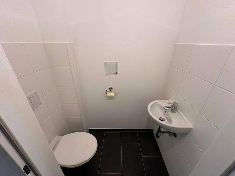 Modernes Gäste-WC mit weiß gefliesten Wänden und dunklem Boden, ausgestattet mit Toilette und Waschbecken.