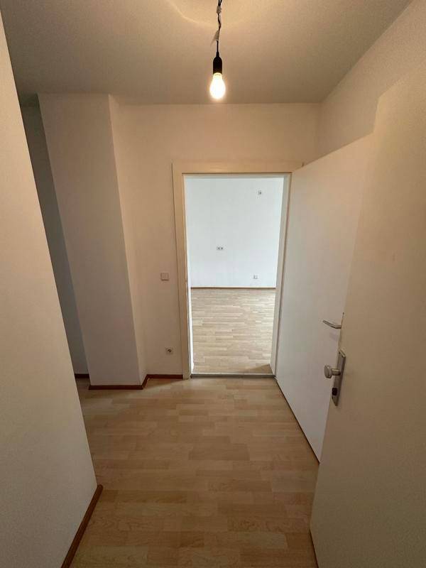 Heller Flur mit Laminatboden und offener Tür, die zu einem weiteren Raum führt.