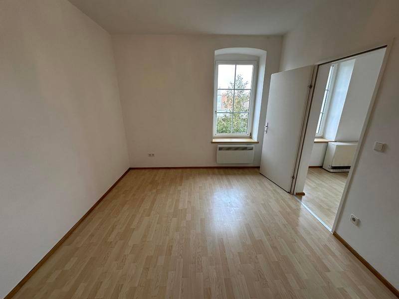 Kleiner, heller Raum mit Laminatboden und einem Fenster mit Blick ins Grüne.