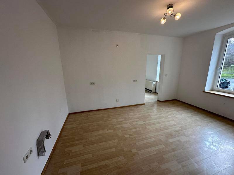 Geräumiger, leerer Raum mit Laminatboden und Blick auf die Straße durch das Fenster.